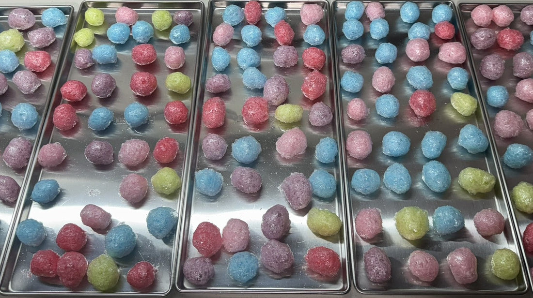 Colorful freeze-dried candy balls in pink, blue, green, and purple on metal trays