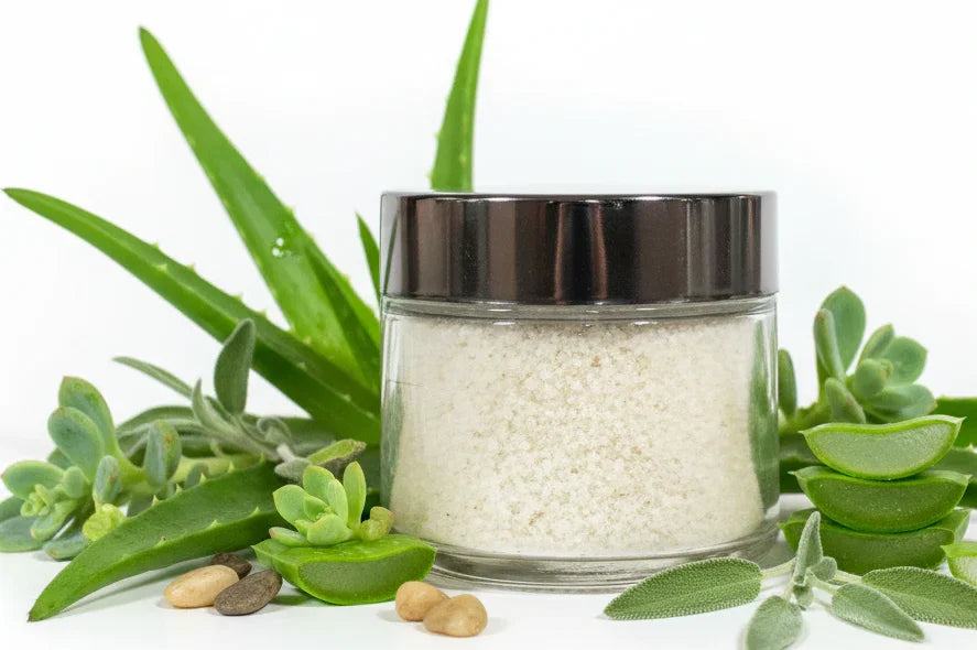 Glass jar of cactus bath salts with black lid, surrounded by aloe and succulents